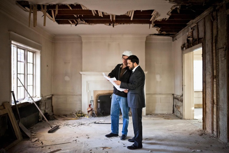 Abbruchkosten Zwei Männer sehen sich einen Plan an, sie stehen im inneren eines baufälligen Hauses