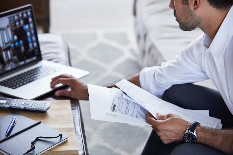 Immobilienverkauf: besser vermietet oder unvermietet verkaufen? - Makler mit Verkauf beauftragen Makler hat alle Formulare für den Verkauf in der Hand und sitzt am Laptop
