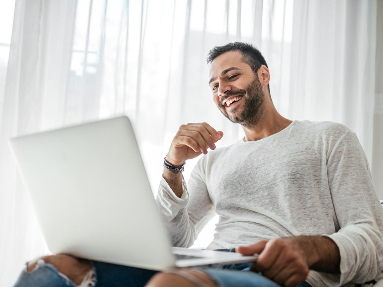 Älterer Mann sitzt vor seinem Computer in seinem Wohnzimmer und überlegt
